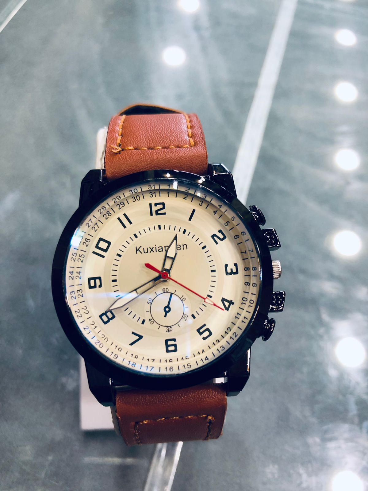 Wristwatch with brown leather strap and beige dial on a reflective surface