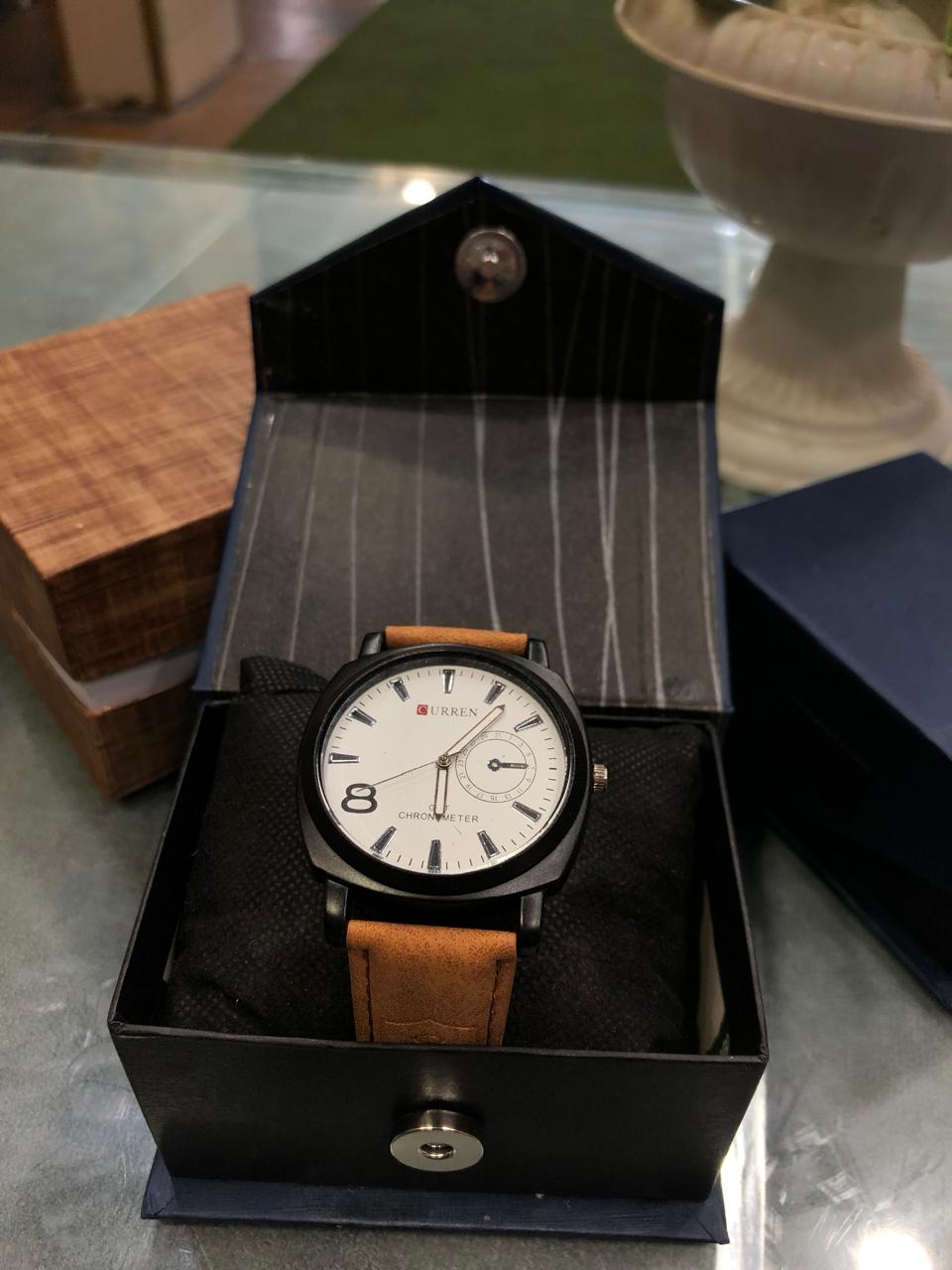 Watch with brown leather strap in a black box on a reflective surface