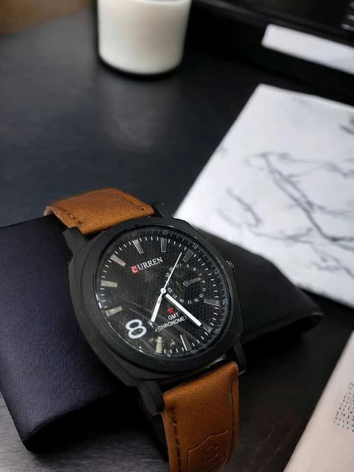 Black watch with brown leather strap on a dark surface