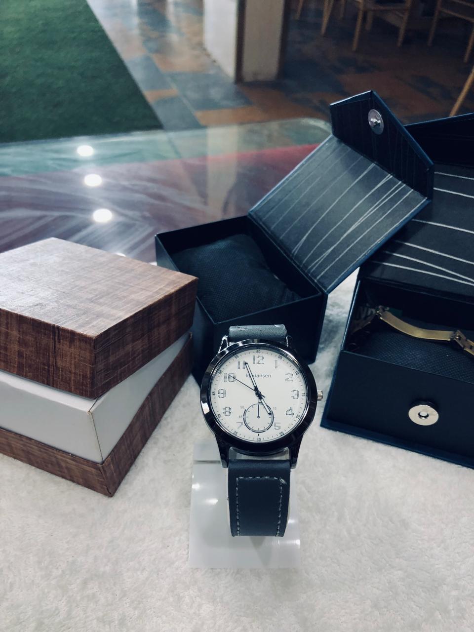 Wristwatch with black strap on a reflective surface, surrounded by open boxes.